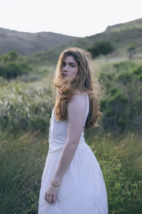 Woman in a white dress standing in tall grass at dusk